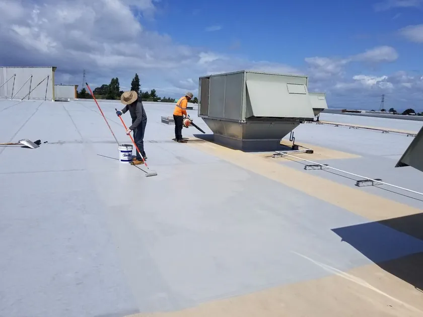 Crew applying elastomeric coating across a flat roof
