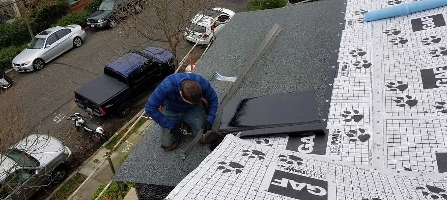 Roofer laying synthetic underlayment across a stripped roof deck above the bay