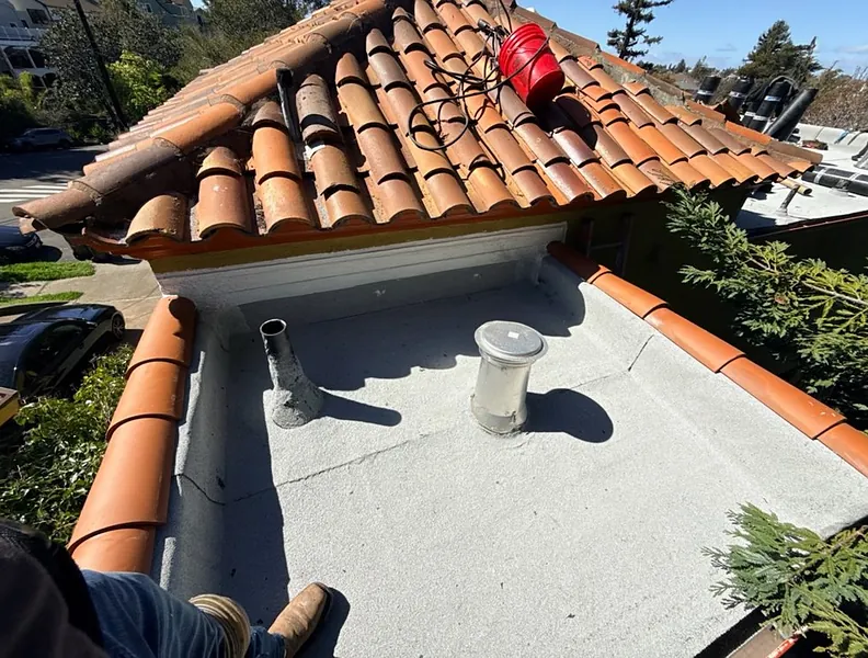 Roofer setting terracotta tiles into fresh flashing on a Bay Area home